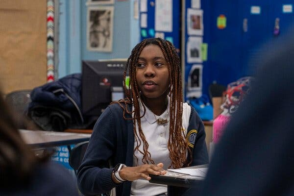 A student in a white shirt and blue sweater seated at a shared work table.