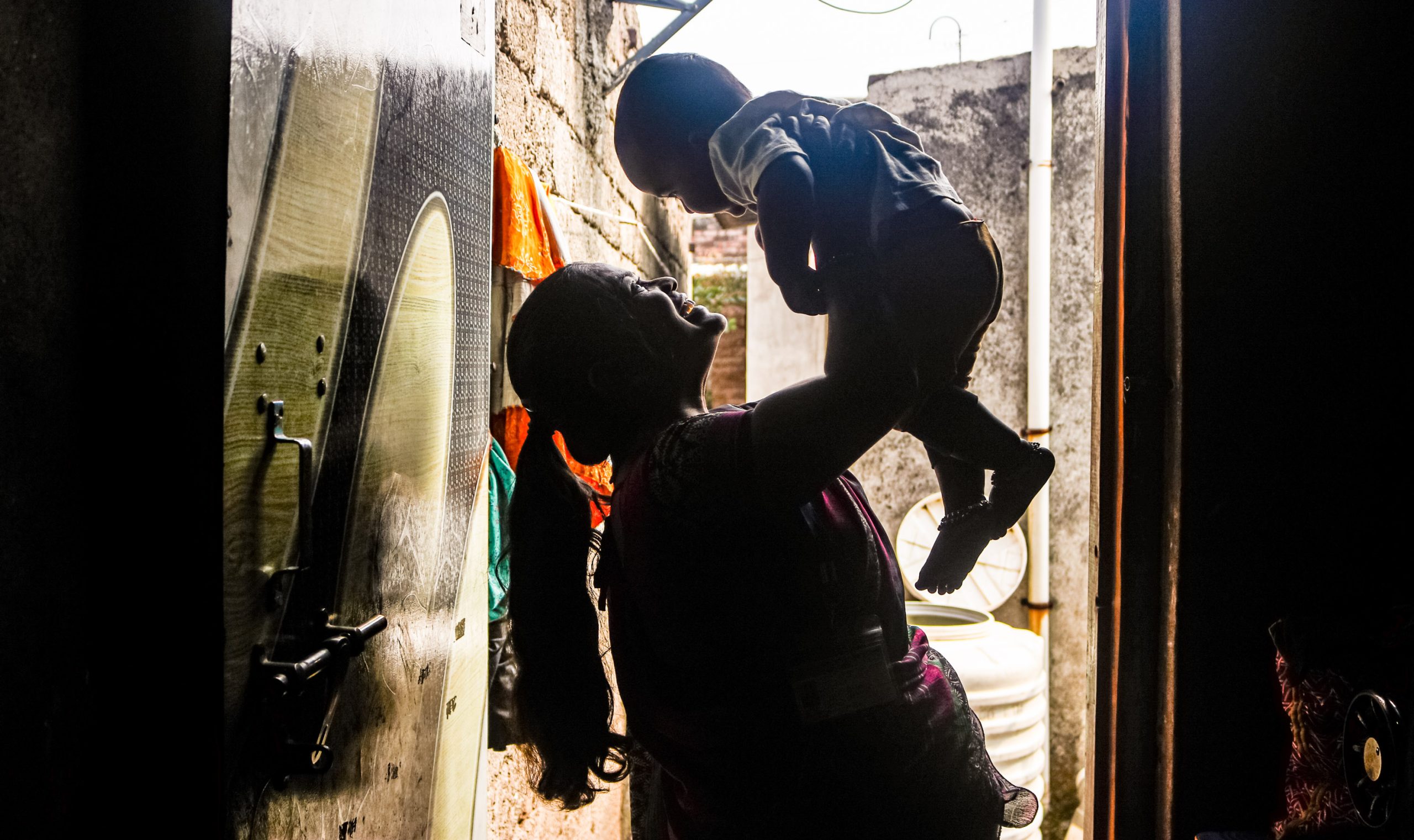 A smiling woman playfully lifts a toddler up in the air