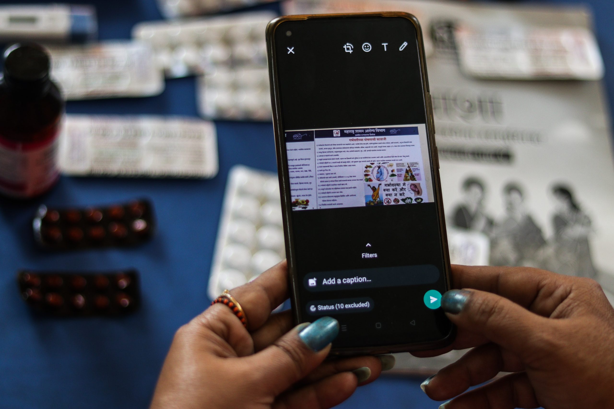 Hands holding a cell phone with a medical brochure on the screen.  Various medicines seen on the table in the background.