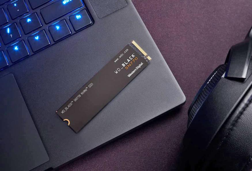 A WD Black SSD on top of a laptop with headphones in the background.