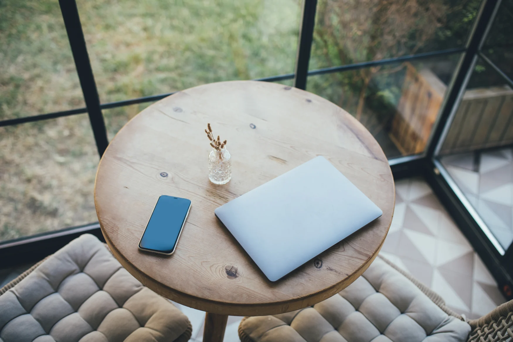 Laptop and smartphone on round wooden table in cozy interior.