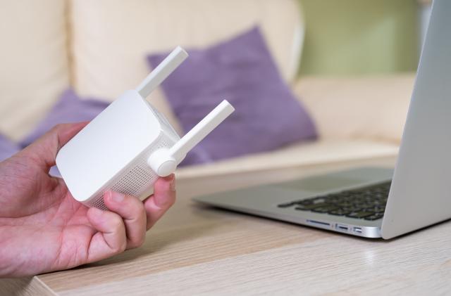 Selective focus at range extender. Internet router on working table with blurred man connect the cable at the background. Fast and high speed internet connection to cover home network usage.