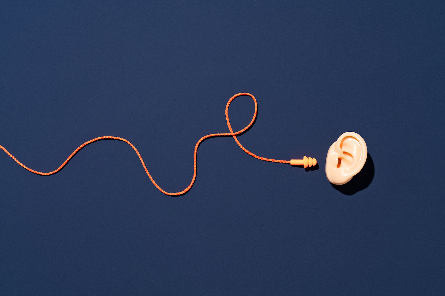 Orange Ear Plugs with Curved String Reach to Ear on Blue Background Directly above View. 4 tips for RevOps teams to filter out the noise and focus on the big picture