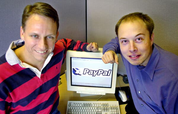Peter Thiel, wears a blue-and-red striped polo, and Elon Musk, a blue collared shirt, in an old photo. Both are resting their arms on a computer whose screen that shows an enlarged PayPal logo.