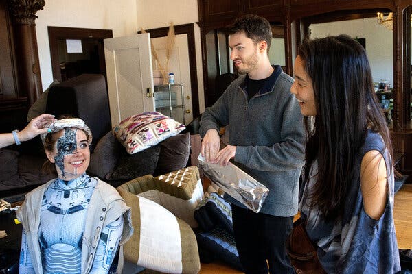 Michaela Carmein getting dressed as a robot. Lucas Gaylord and Emily Liu stand next to Carmein.