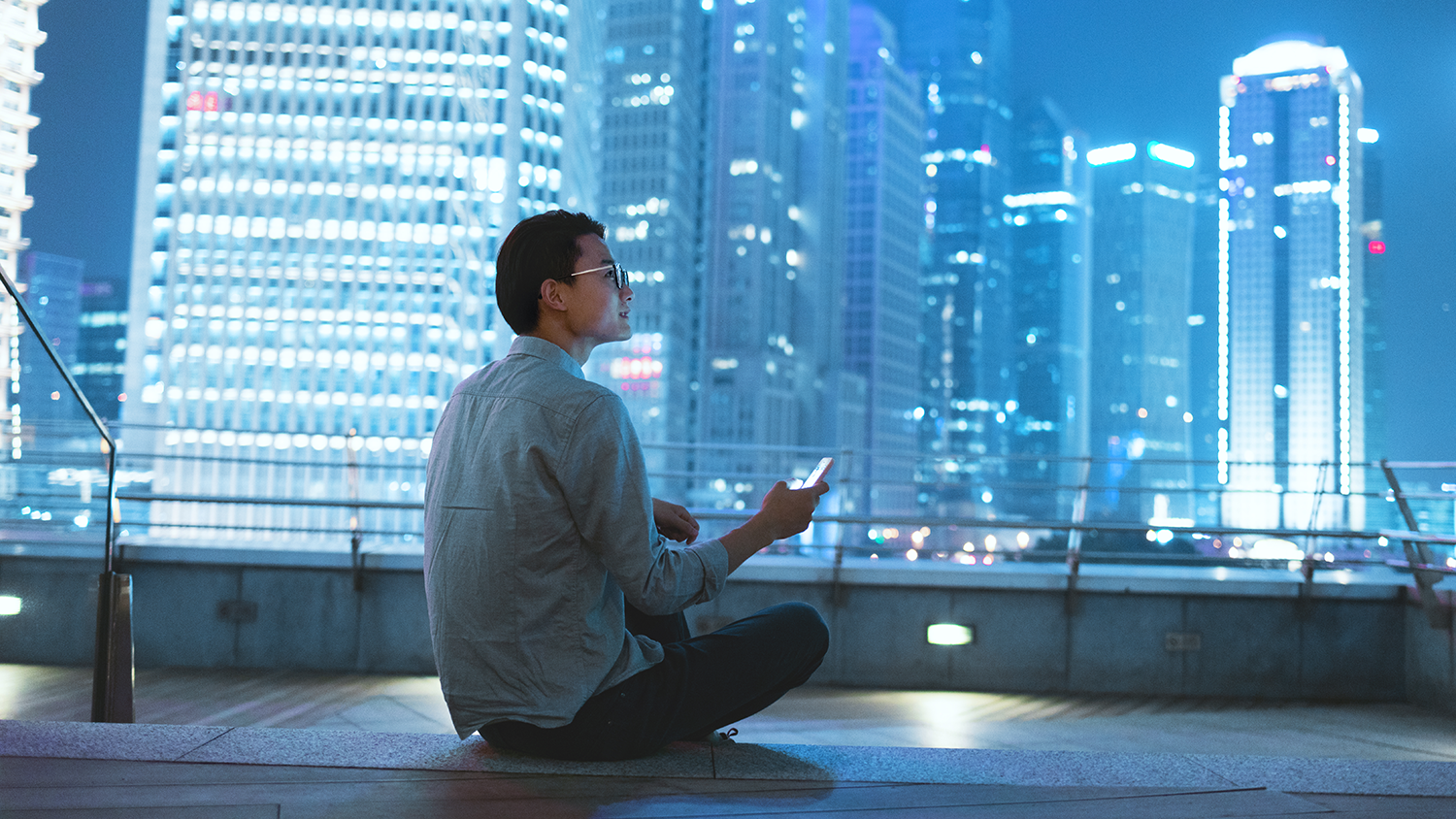 stock image of man sitting on a rooftop deck with a cellphone.