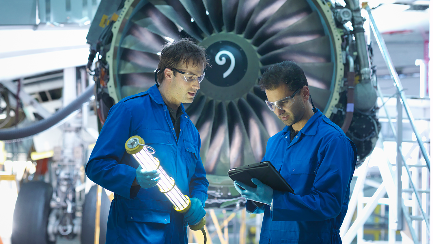 Stock image of two scientists in a machine shop reviewing info on a tablet