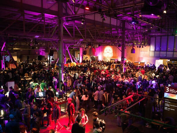 A large space with crowds of people gathered under purple lights.