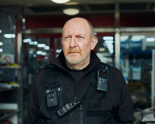 A portrait photo of Mr. Mackenzie with a phone and other security gear attached to the front of his jacket.