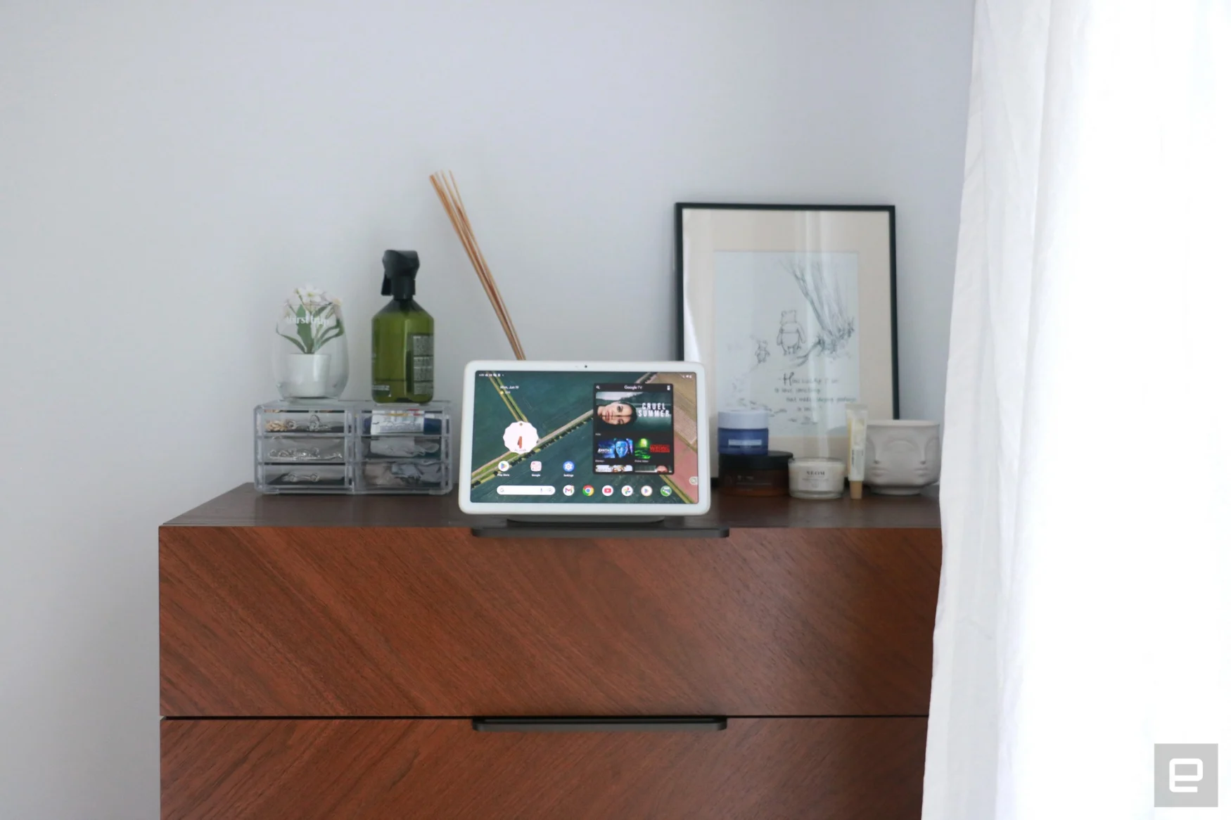 The Pixel Tablet on a walnut dresser, with various items behind it. The top two drawers are in view.