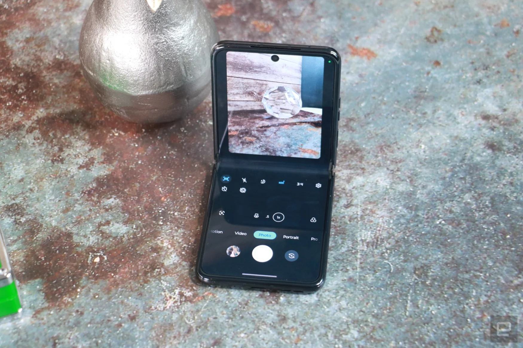 Top down view of the Motorola Razr+ half folded and propped up on a surface with its internal  screen facing out. On the display is the camera interface, with the viewfinder on the top half showing a bronze pear and the bottom half is dedicated to controls like the shutter button and timers.