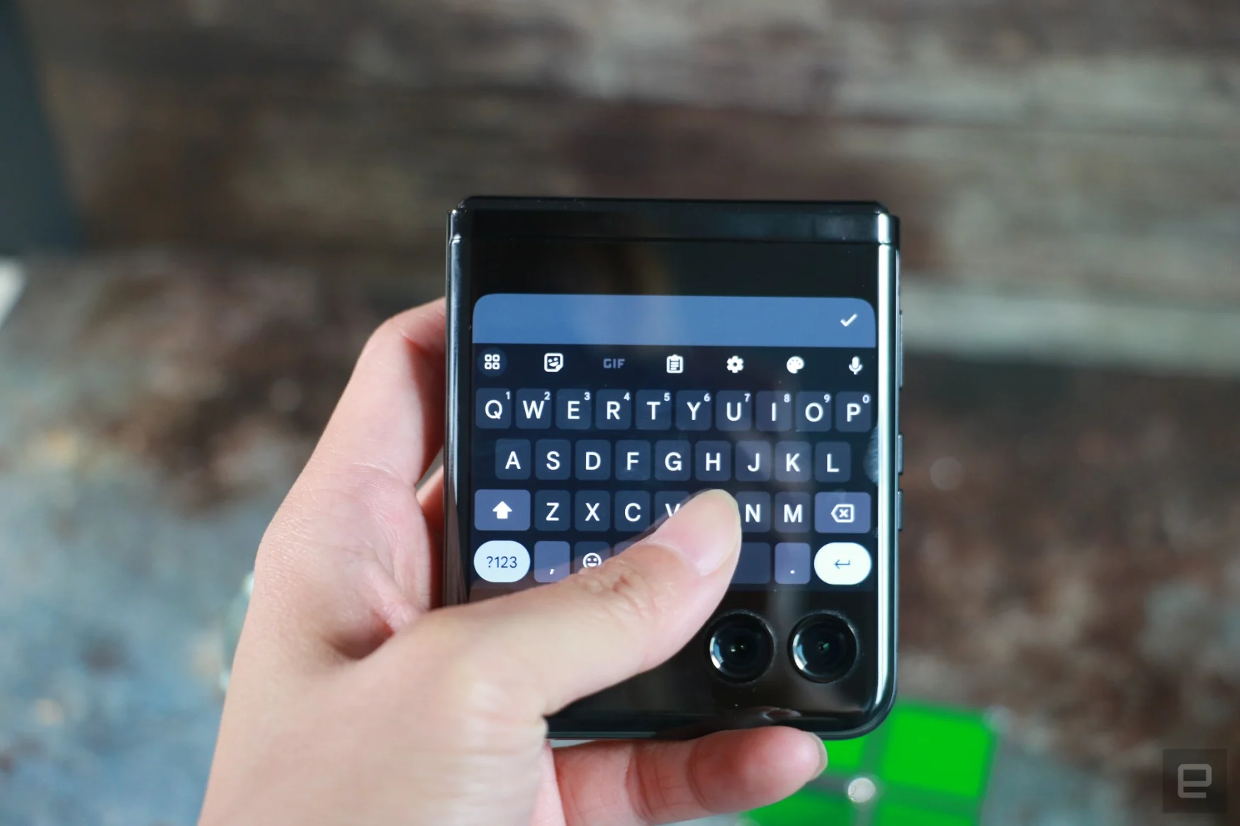 The Motorola Razr+ folded shut and held in mid-air, with a full QWERTY keyboard showing on its external display and a thumb hovering over the space bar.