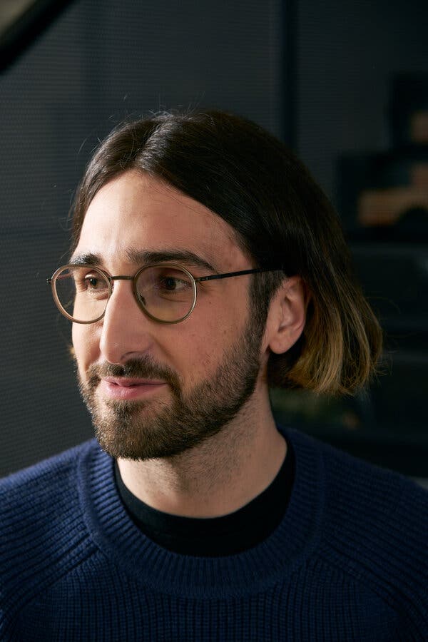 A man with long hair, a beard and glasses poses for a photo.