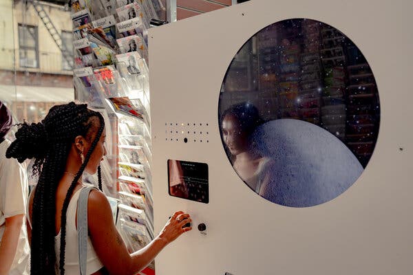 A woman with long dark braided hair, who is wearing a white tank top, seen from the side turning a black knob on the front of a white machine with blinking lights, black buttons and screens on its front. 