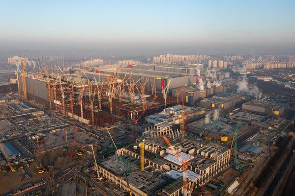 An aerial view of cranes at a construction site, with apartment towers in the distance.