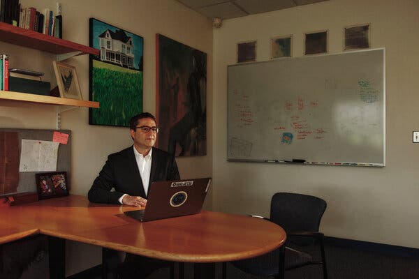 Brian Levine, wearing glasses and a suit, sits behind a desk with a laptop in front of him. 