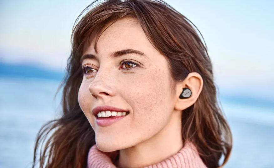 A lady wearing earbuds on the beach living life to the fullest.