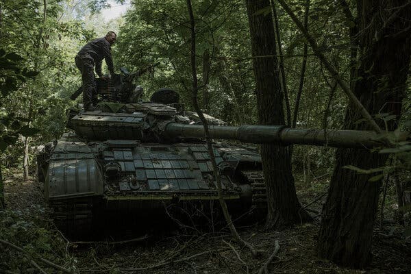 A Ukrainian soldier loads ammunition on a tank in a wooded area.
