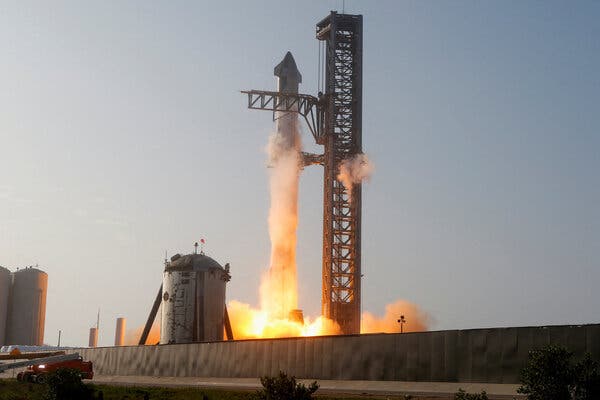 A view of the extremely tall Starship rocket at the launchpad as its engines ignite.