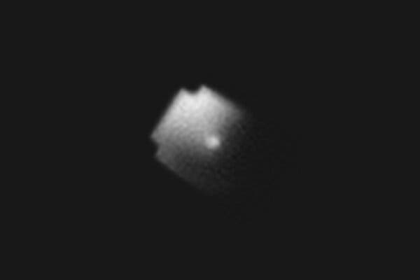 A telescope image of the Bluewalker3 satellite, which looks like a square with small indentations on its corners with a bright dot in its center, half-cached in darkness.