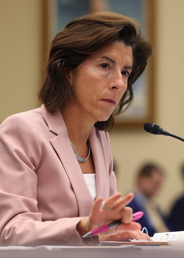 Commerce Secretary Gina Raimondo, wearing a pink suit, sits a witness table during a Congressional hearing.