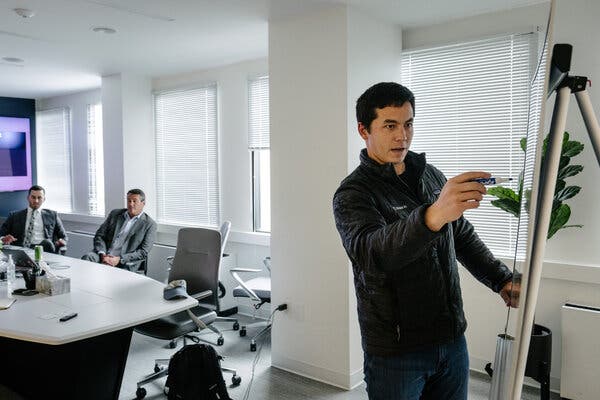 Brandon Tseng writing on a whiteboard in a conference room while two men in suits, seated at a table, look on.