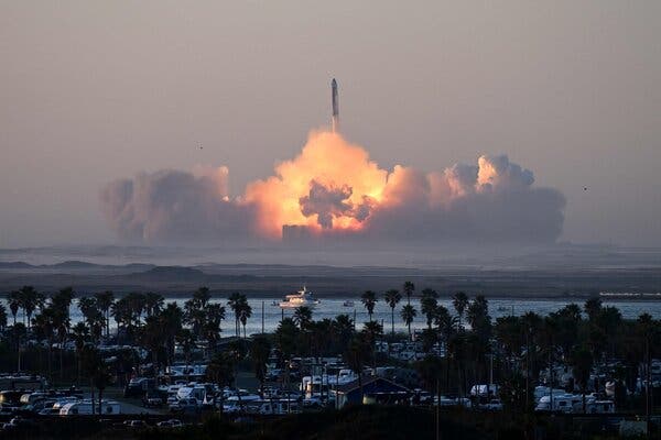 SpaceX’s Starship rocket rises with its flame lightining up a cloud it created. The rocket is in the background and the foreground is filled with palm trees and camper vans.