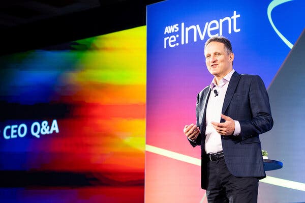 Adam Selipsky speaks in front of a colorful screen that says “A.W.S. re: Invent.”