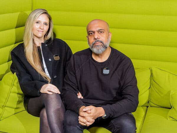 Bethany Bongiorno and Imran Chaudhri, both wearing black, are sitting close to each other on a lime green sofa. They are both wearing small squared pins on their tops.