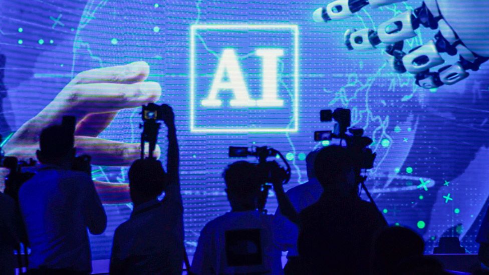 The letters AI on a giant screen as people look on