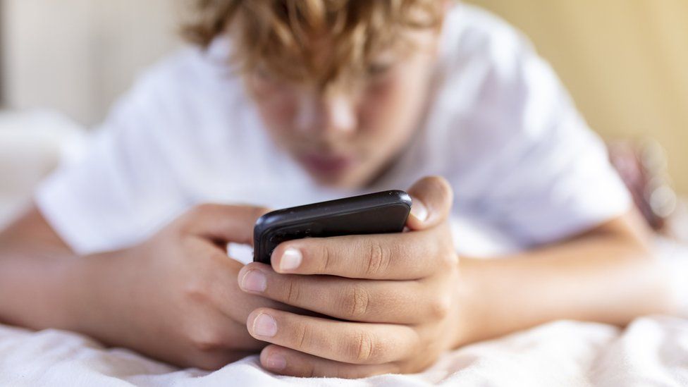 a teen holding smart phone in bed