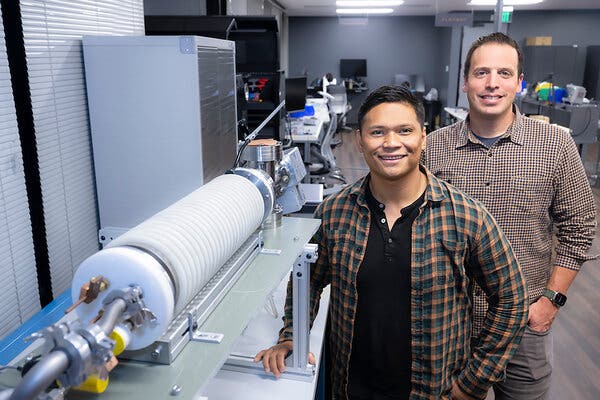 Two men stand in a lab next to a large piece of sophisticated equipment.