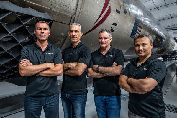 A group portrait of Michael López-Alegría, Marcus Wandt, Walter Villadei and Alper Gezeravci in front of a large rocket on its side in a hangar.